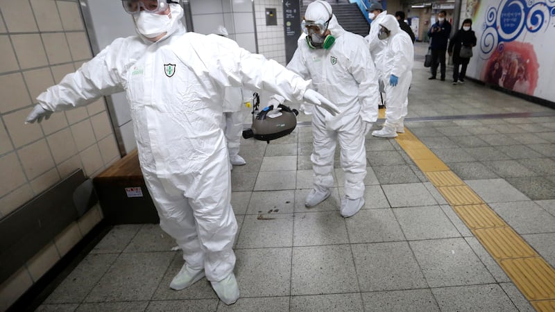 Workers wearing protective gears help clean each other's suits after disinfecting as a...